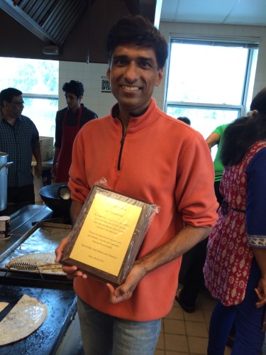 Hasmukhbhai holds an appreciation plaque recognizing his Shala kitchen service.